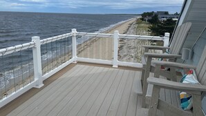 A wooden deck with a white railing overlooking a beach.