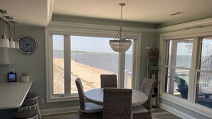 A dining area with a view of the beach, wicker chairs, a round table, and a chandelier.