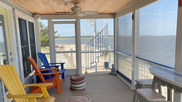 A covered deck with wooden flooring, a ceiling fan, and a view of the water.