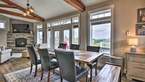 A dining area with a wooden table and chairs, a stone fireplace, and large windows offering a view of the outdoors. - 'traveler's Retreat' Studio w/ Patio & Yard! (Tualatin)
