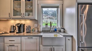 A modern kitchen with white cabinets, a stainless steel refrigerator, and a window with a view of trees and a house. - 'traveler's Retreat' Studio w/ Patio & Yard! (Tualatin)