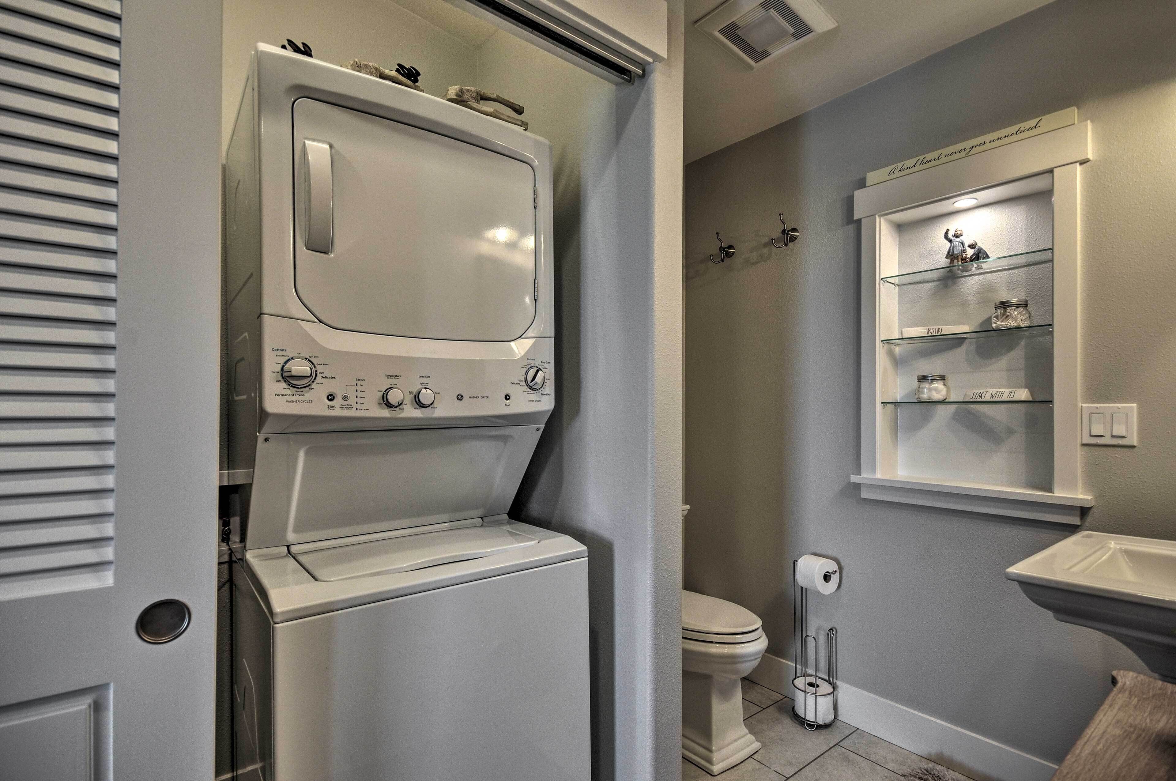 Ein kleiner Hauswirtschaftsraum mit einer Waschmaschine und einem Trockner mit Frontöffnung, einer Toilette und einem kleinen Regal mit Dekoration.