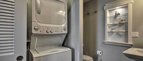 Ein kleiner Hauswirtschaftsraum mit einer Waschmaschine und einem Trockner mit Frontöffnung, einer Toilette und einem kleinen Regal mit Dekoration.