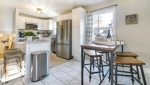 A modern kitchen with white cabinets, stainless steel appliances, and a wooden dining table with stools. - Sunny Family Home, 3 Mi to High Point Market! (High Point)
