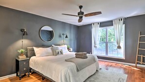 Ein Schlafzimmer mit Bett, Nachttischlampen, Deckenventilator, Fenster mit Vorhängen und einer Holzleiter.