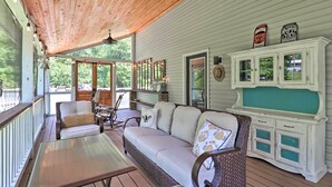Eine überdachte Veranda mit Holzboden, einer gepolsterten Couch, Korbsesseln, einem Tisch und einer Vitrine.