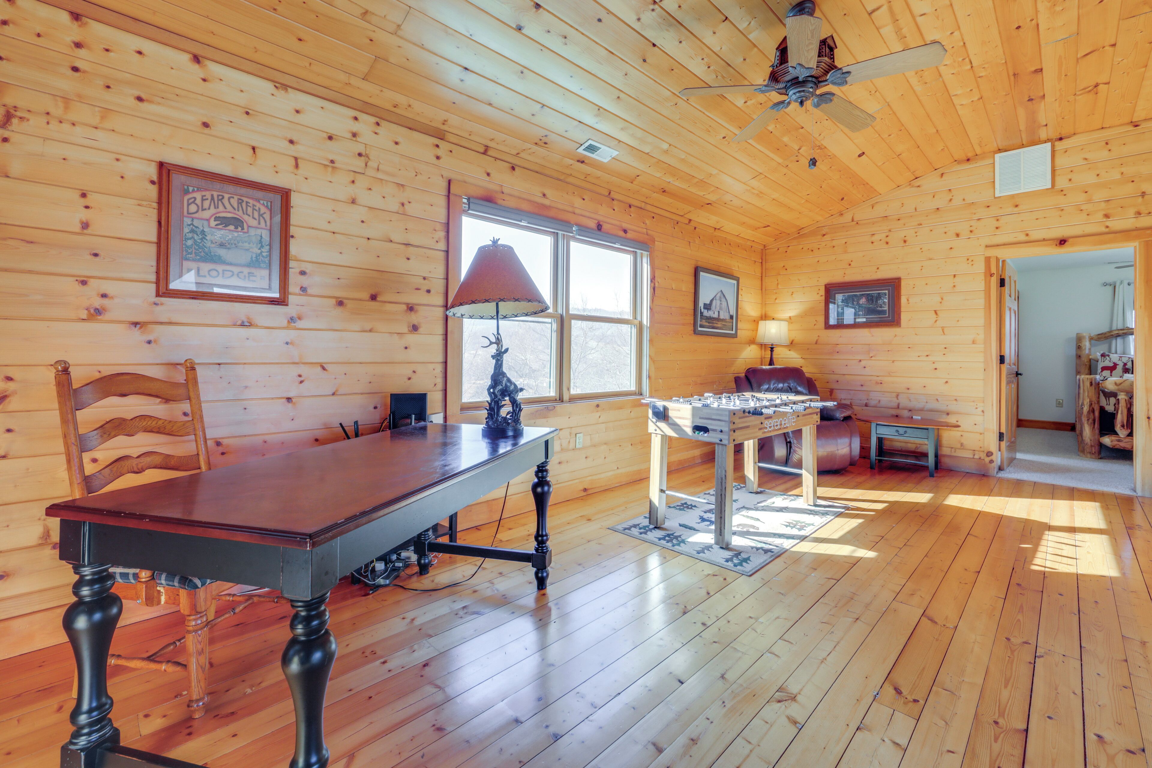 L’intérieur d’un chalet en bois comprend une table à manger, des chaises, une lampe, un baby-foot et un ventilateur de plafond.