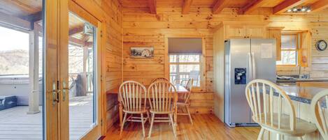 A wooden cabin interior with a dining area, kitchen, and a large window.