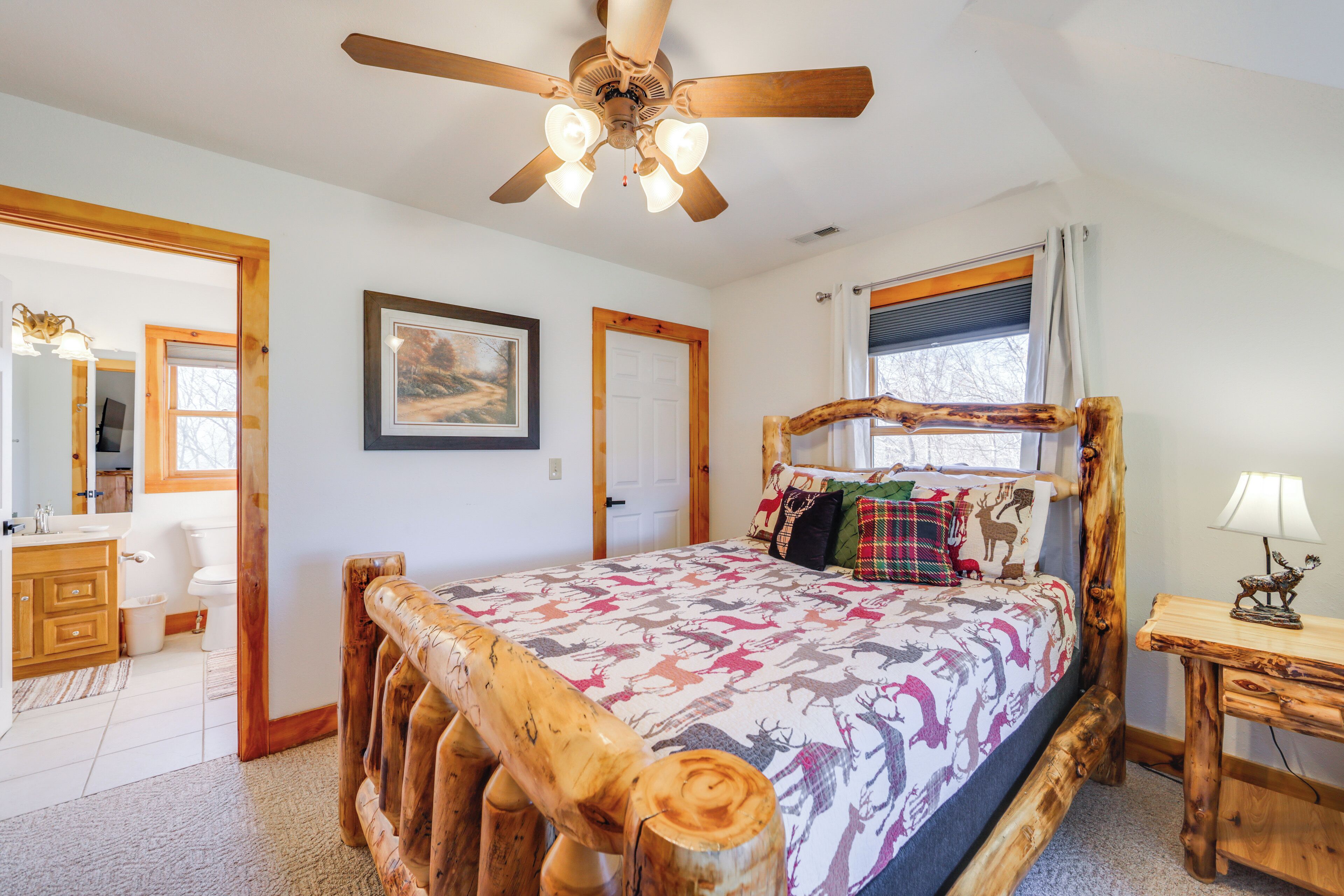 A bedroom with a wooden bed frame, a ceiling fan, a window with curtains, and a bedside table with a lamp.