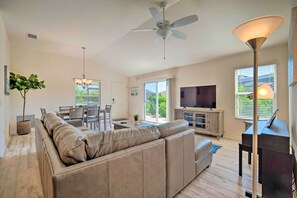 Un salon moderne avec un canapé en cuir beige, un coin repas comprenant une table et des chaises, un ventilateur de plafond et un téléviseur.