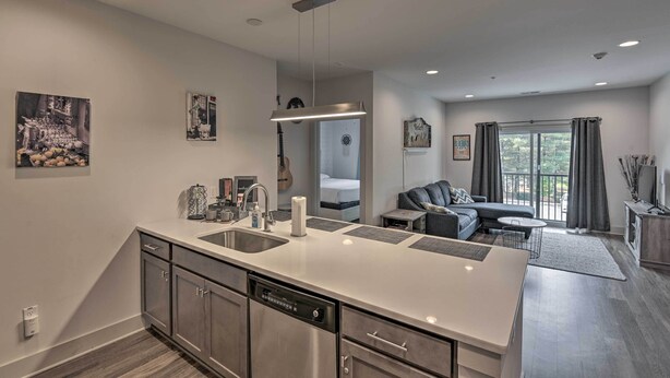 A modern kitchen with a central island, a dining area with a sofa and table, and a bedroom with a large window. - Modern Nashville Condo: 7 Mi to Downtown! (Nashville)