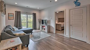 A modern living room with a sofa, a coffee table, and a TV. There is a door leading to a kitchen and a balcony. - Modern Nashville Condo: 7 Mi to Downtown! (Nashville)