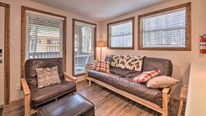 A cozy living room with a leather sofa, wooden armchairs, and a bench. There are large windows with blinds, a lamp, and a fire extinguisher on the wall. - Angel Fire Mountainside Condo < 1/2 Mi to Slopes (Angel Fire)