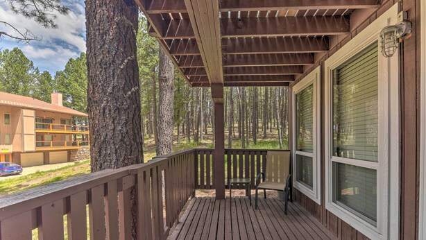 A wooden deck with a bench, a large tree, and a building with a balcony in the background. - Angel Fire Mountainside Condo < 1/2 Mi to Slopes (Angel Fire)
