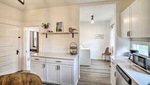 A modern kitchen with white cabinetry, a built-in dishwasher, and a microwave. There is a wooden stool in the foreground and a chair in the background. - Cozy Eclectic Home ~ 1 Mi to Downtown Spokane (Spokane)