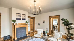 A spacious living room with a fireplace, wooden flooring, and a chandelier. There are two white armchairs and a round coffee table. - Cozy Eclectic Home ~ 1 Mi to Downtown Spokane (Spokane)