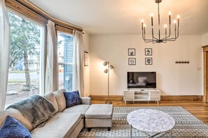 A modern living room with a sofa, ottoman, TV, and chandelier. - Cozy Eclectic Home ~ 1 Mi to Downtown Spokane (Spokane)