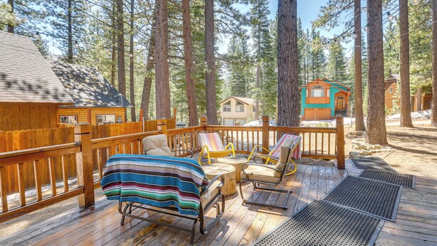 A wooden deck with outdoor seating and a view of a forested area. - Tahoe Home in the Pines: Quiet Neighborhood! (South Lake Tahoe)
