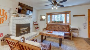 A living room with a fireplace, leather sofa, wooden coffee table, and a ceiling fan. - Tahoe Home in the Pines: Quiet Neighborhood! (South Lake Tahoe)