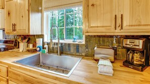 A kitchen with wooden cabinets, a stainless steel sink, a window with a view of trees, a toaster, and a coffee maker. - Tahoe Home in the Pines: Quiet Neighborhood! (South Lake Tahoe)