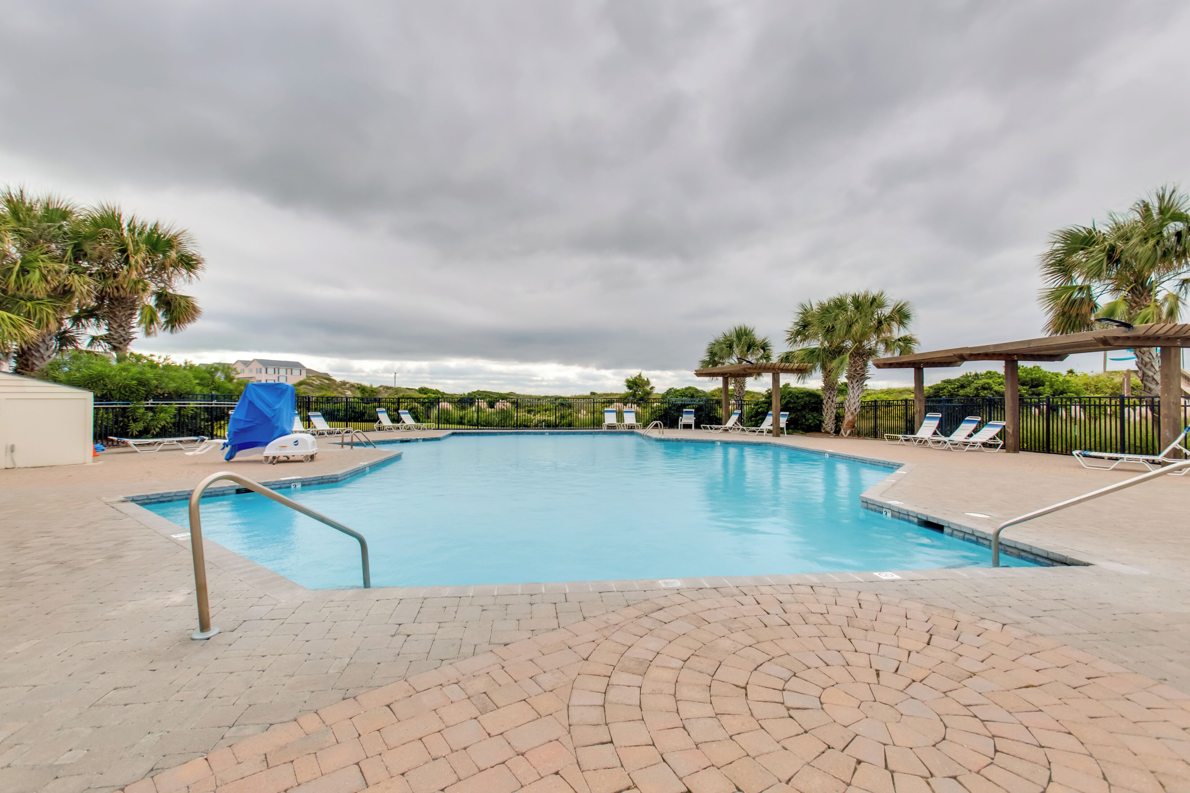 A rectangular swimming pool with a tiled deck, surrounded by palm trees and lounge chairs.