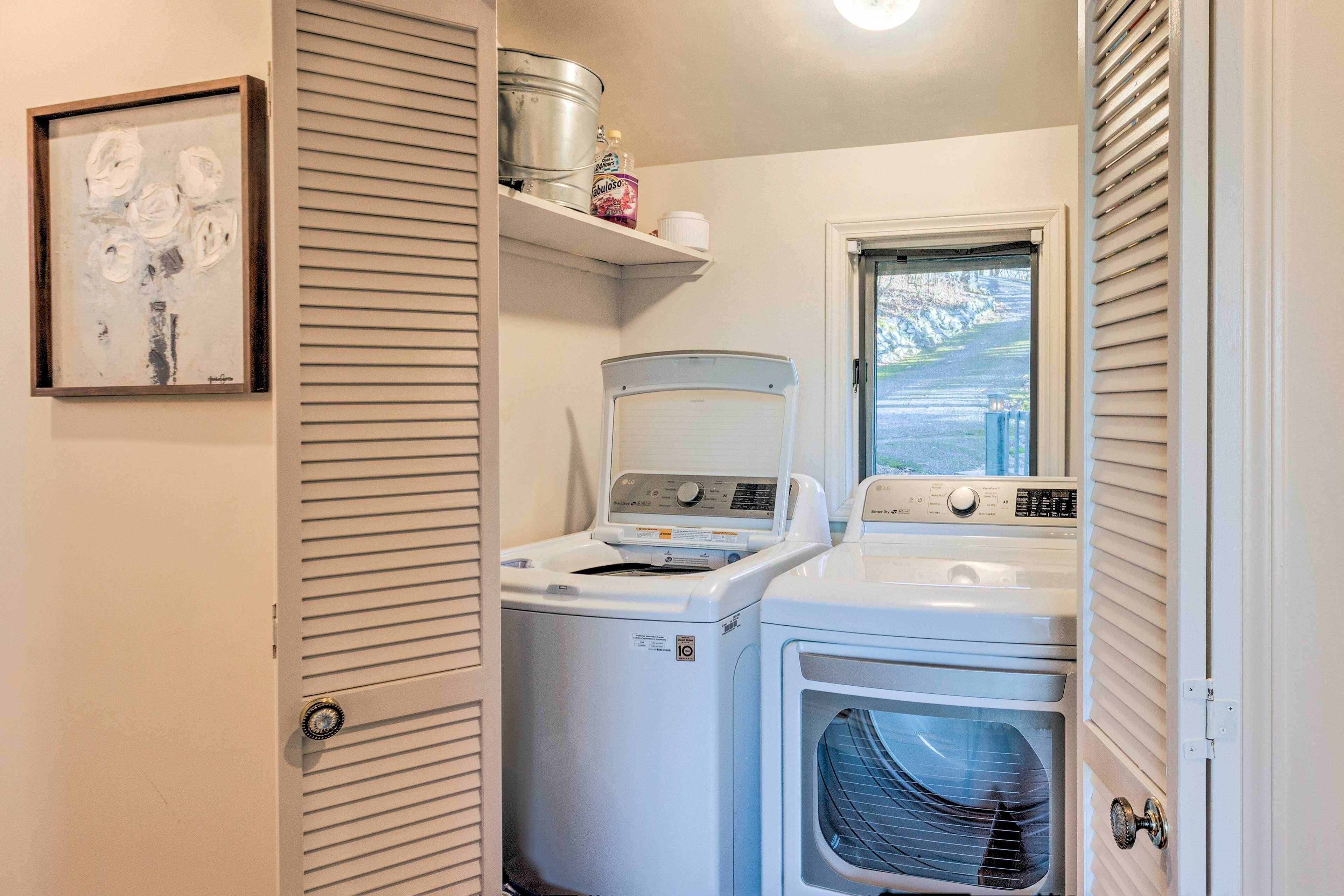 A laundry room with two stacked washers and dryers, a window with blinds, and a shelf with laundry supplies.