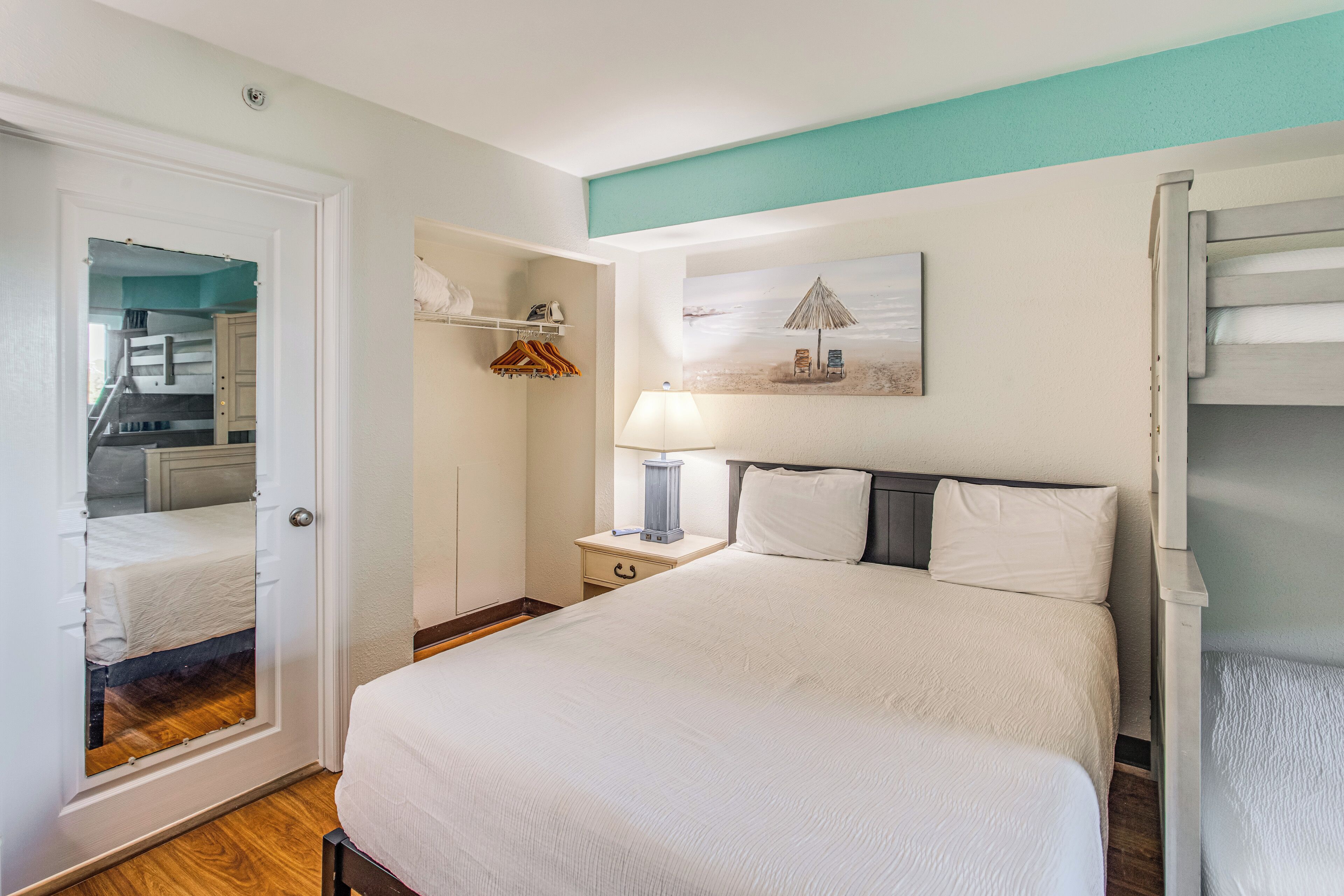 A bedroom with a bed, a nightstand, a lamp, a painting, and a wardrobe.