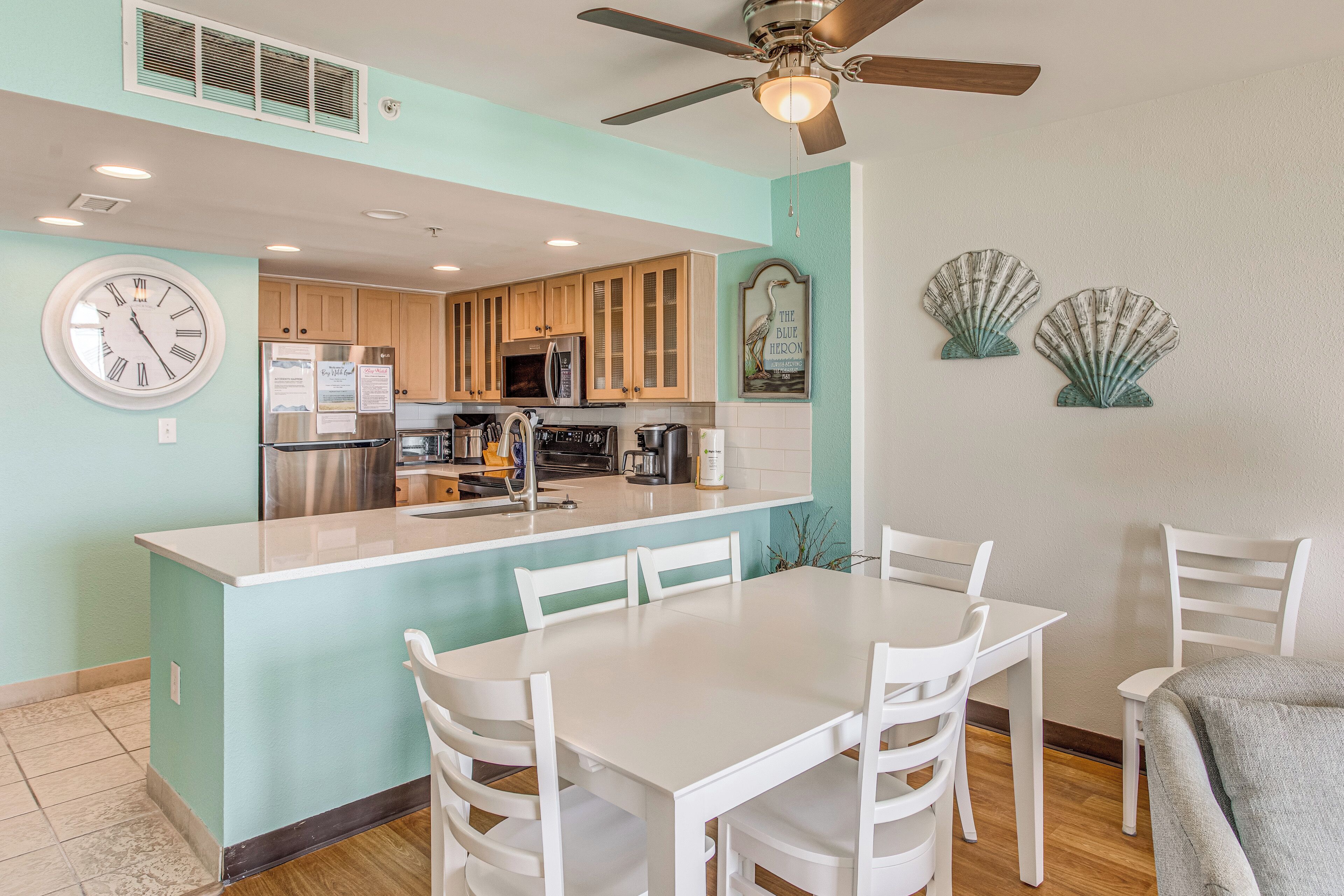 A kitchen with a central island, white chairs, and a ceiling fan.