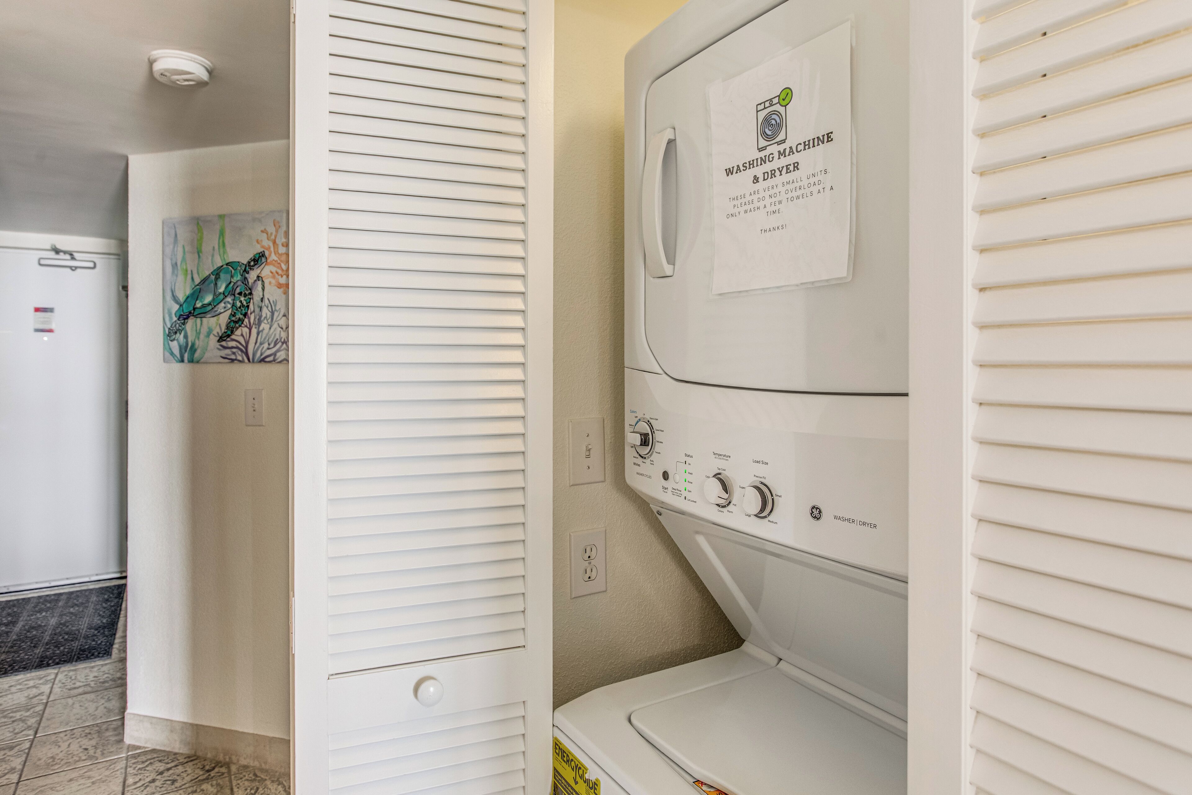 A laundry room with a stacked washer and dryer, a painting on the wall, and a door with a handle.