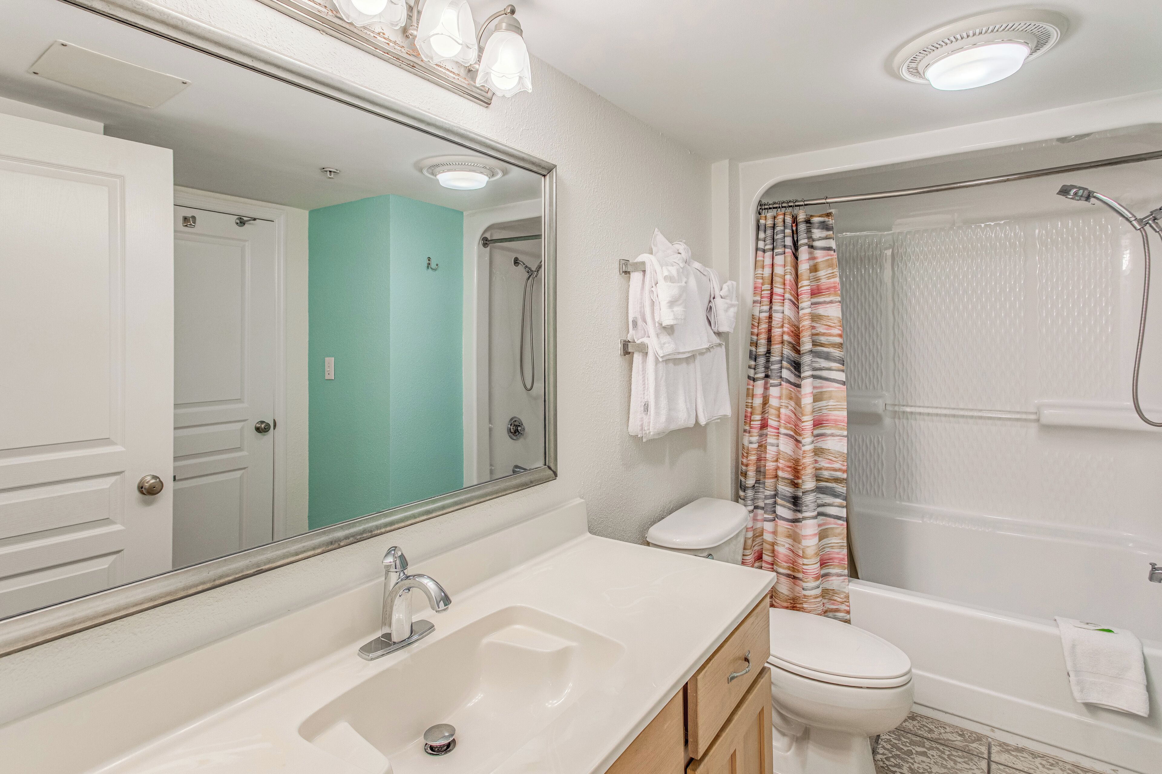 A bathroom with a white sink, mirror, toilet, and shower.