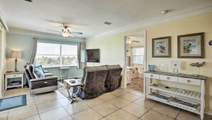 A living room with a sofa, TV, and a console table with decorative items. - St Augustine Condo w/ Pool Access, Walk to Beach! (St. Augustine)