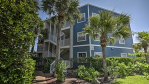 A multi-story building with a blue exterior, a wooden deck, and a palm tree in the foreground. - St Augustine Condo w/ Pool Access, Walk to Beach! (St. Augustine)