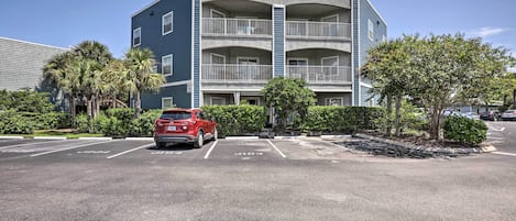 A multi-story building with balconies and a parking lot in front.