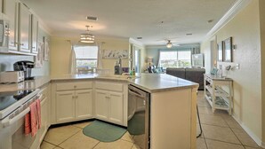 A kitchen with white cabinets, a dishwasher, and a countertop. There is a dining area with a couch and a table. - St Augustine Condo w/ Pool Access, Walk to Beach! (St. Augustine)