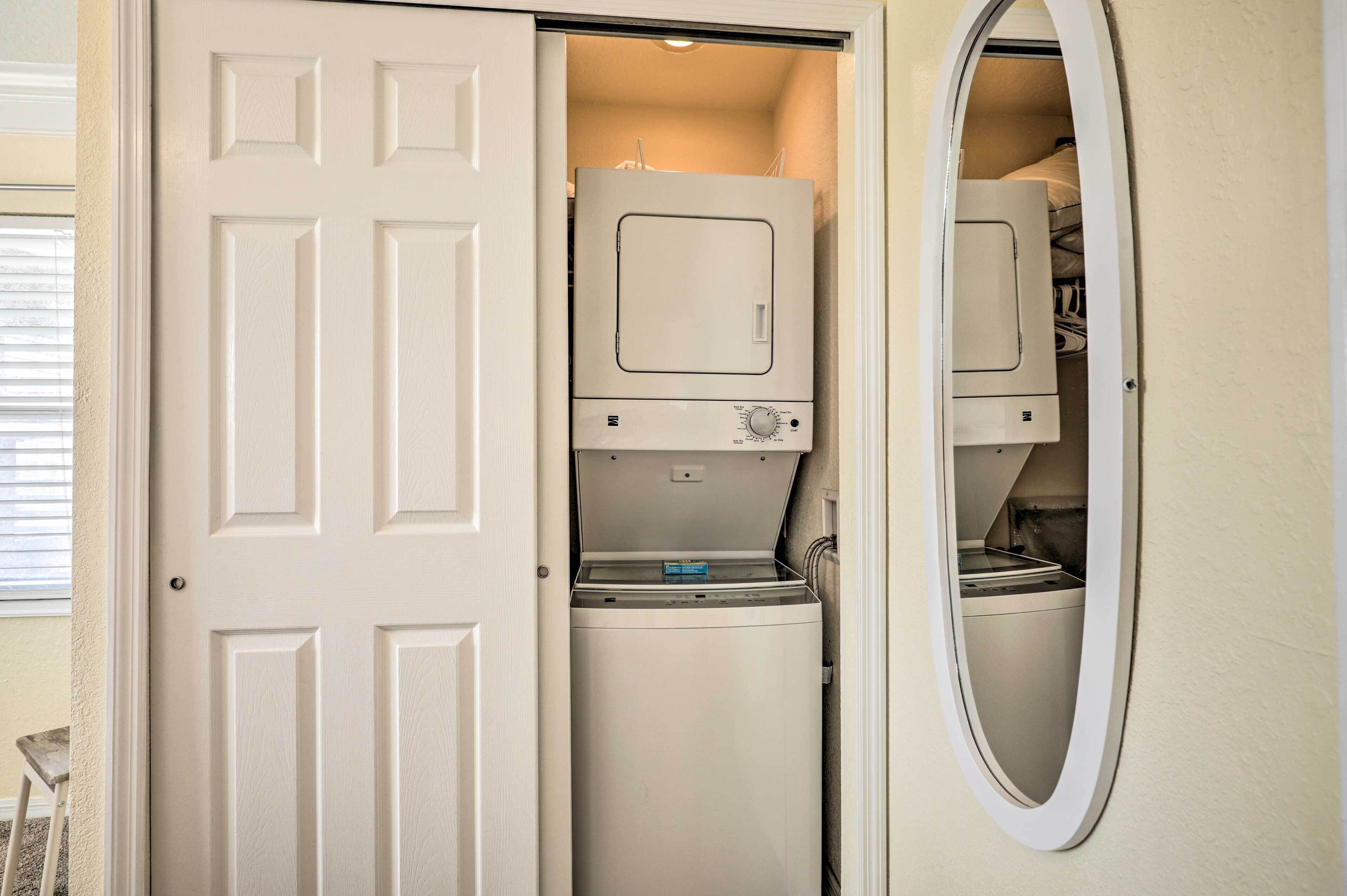 A compact laundry room with a front-loading washer and dryer, a small storage cabinet, and a mirror on the wall.