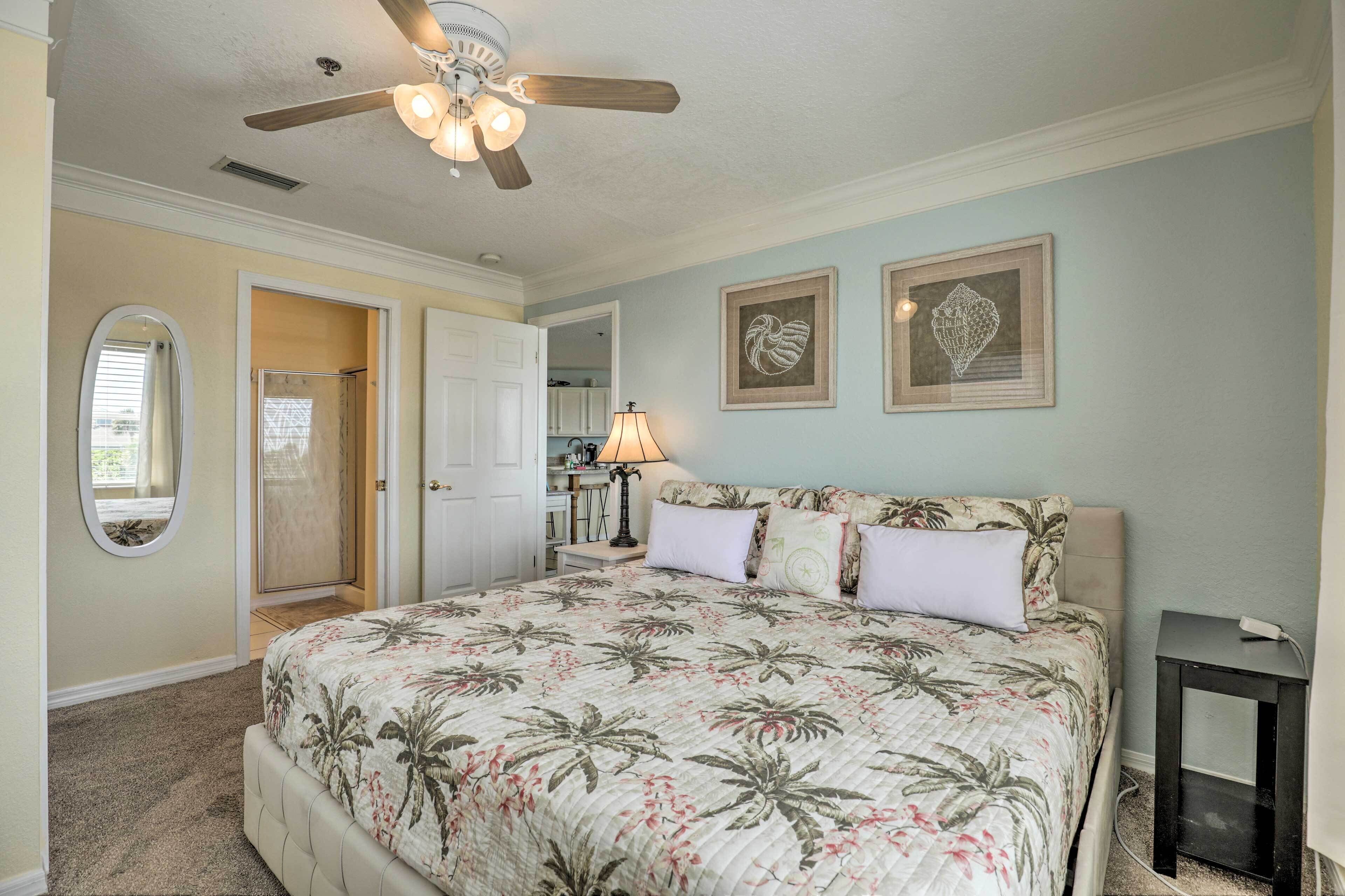 A bedroom with a bed, a ceiling fan, a lamp, and framed artwork on the wall.