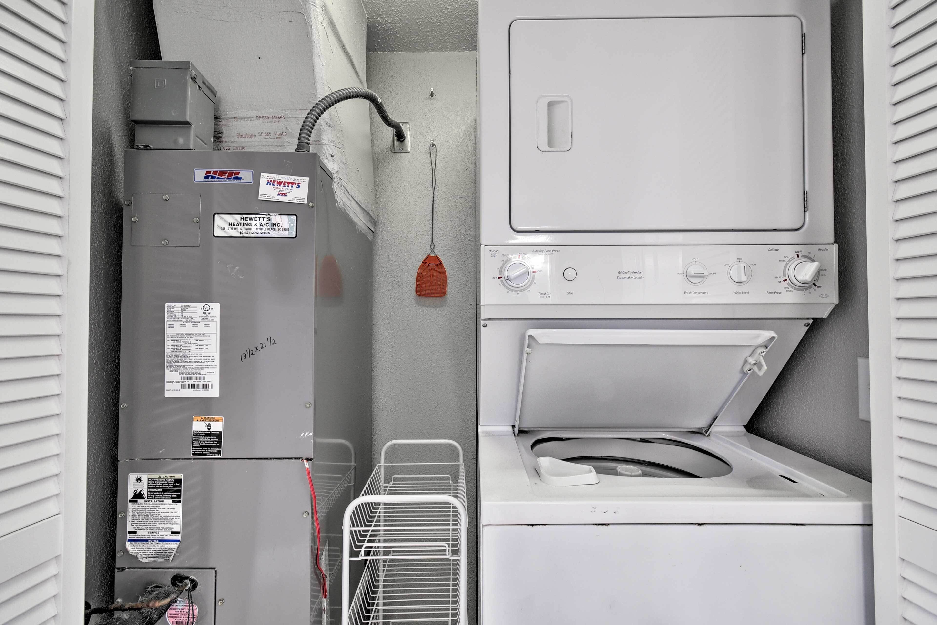 A laundry area with a front-loading washer and dryer, a utility meter, and a metal laundry basket.