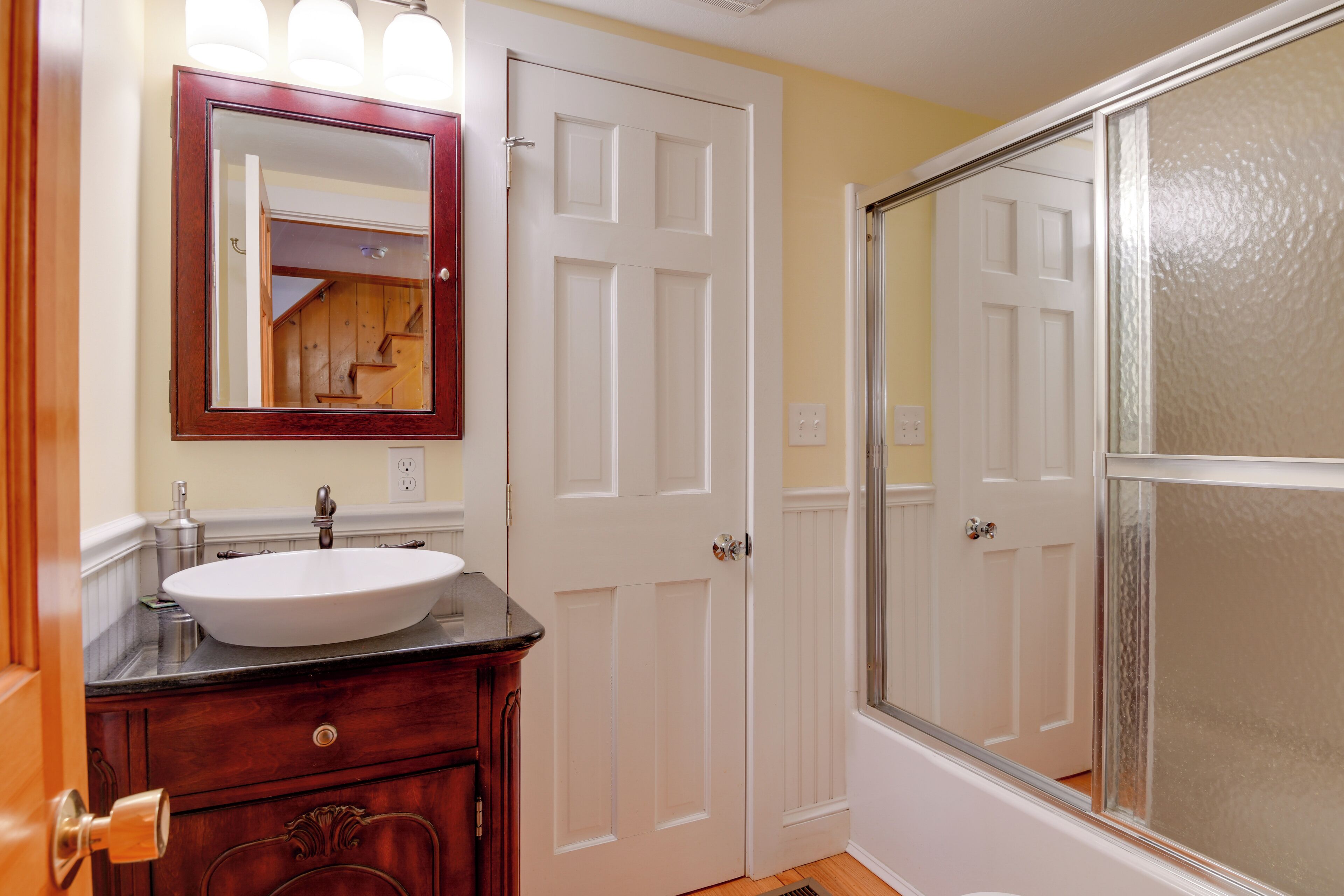 Une salle de bain avec un lavabo blanc, un meuble-lavabo en bois et un miroir avec éclairage intégré.