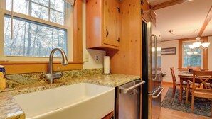 Una cocina con pileta, lavavajillas y refrigerador. Se ve un ventanal con vistas a árboles.