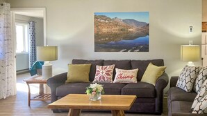 A living room with a dark brown sofa, a wooden coffee table with a vase of flowers, and a painting of a mountainous landscape above the sofa. - Hike, Ski, Explore: Lincoln Condo w/ Pool Access (Lincoln)