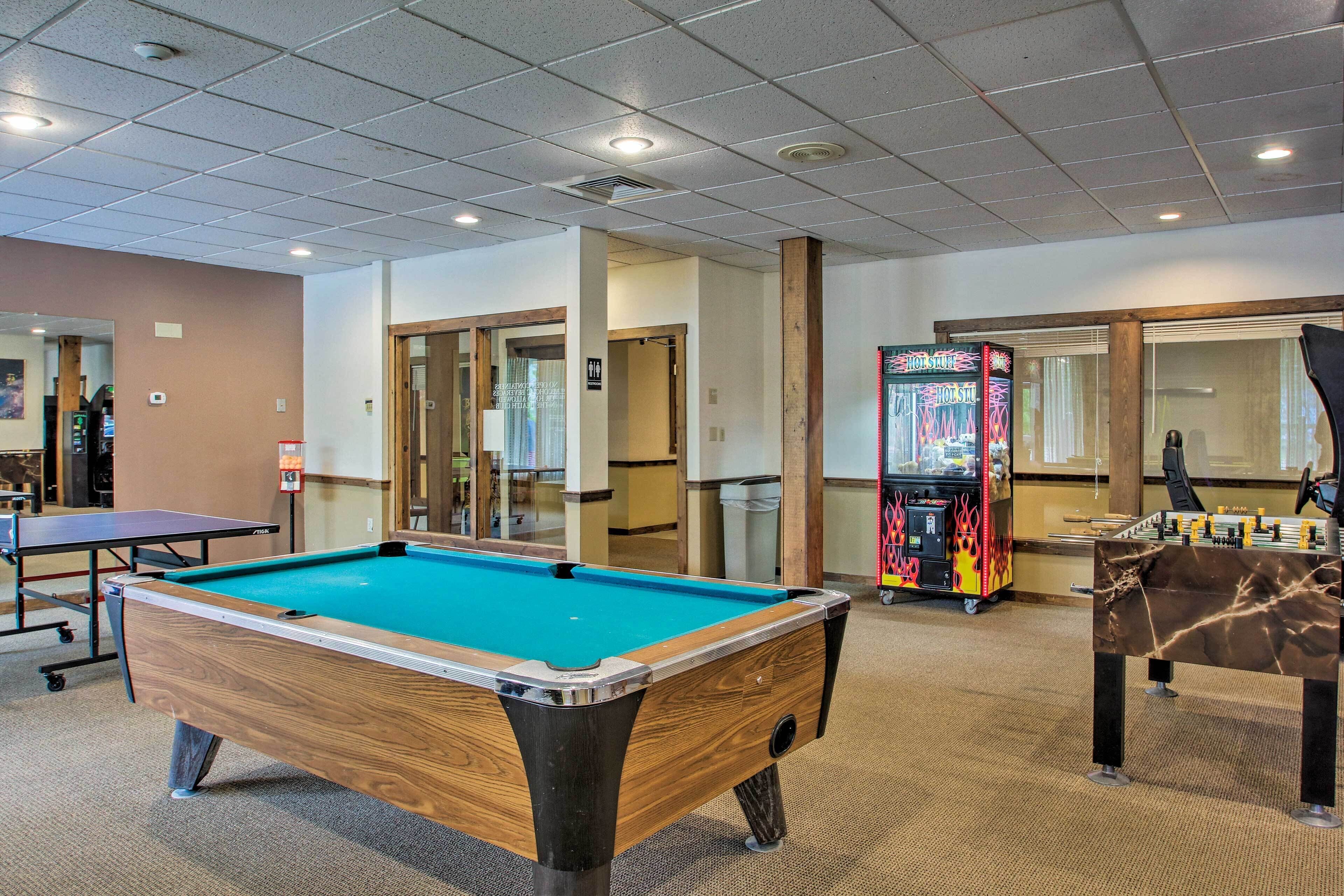 A pool table in a room with a carpeted floor, a ping pong table, and a foosball table.