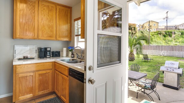 A kitchen with wooden cabinets, a dishwasher, and a view of a backyard with a grill and patio furniture.