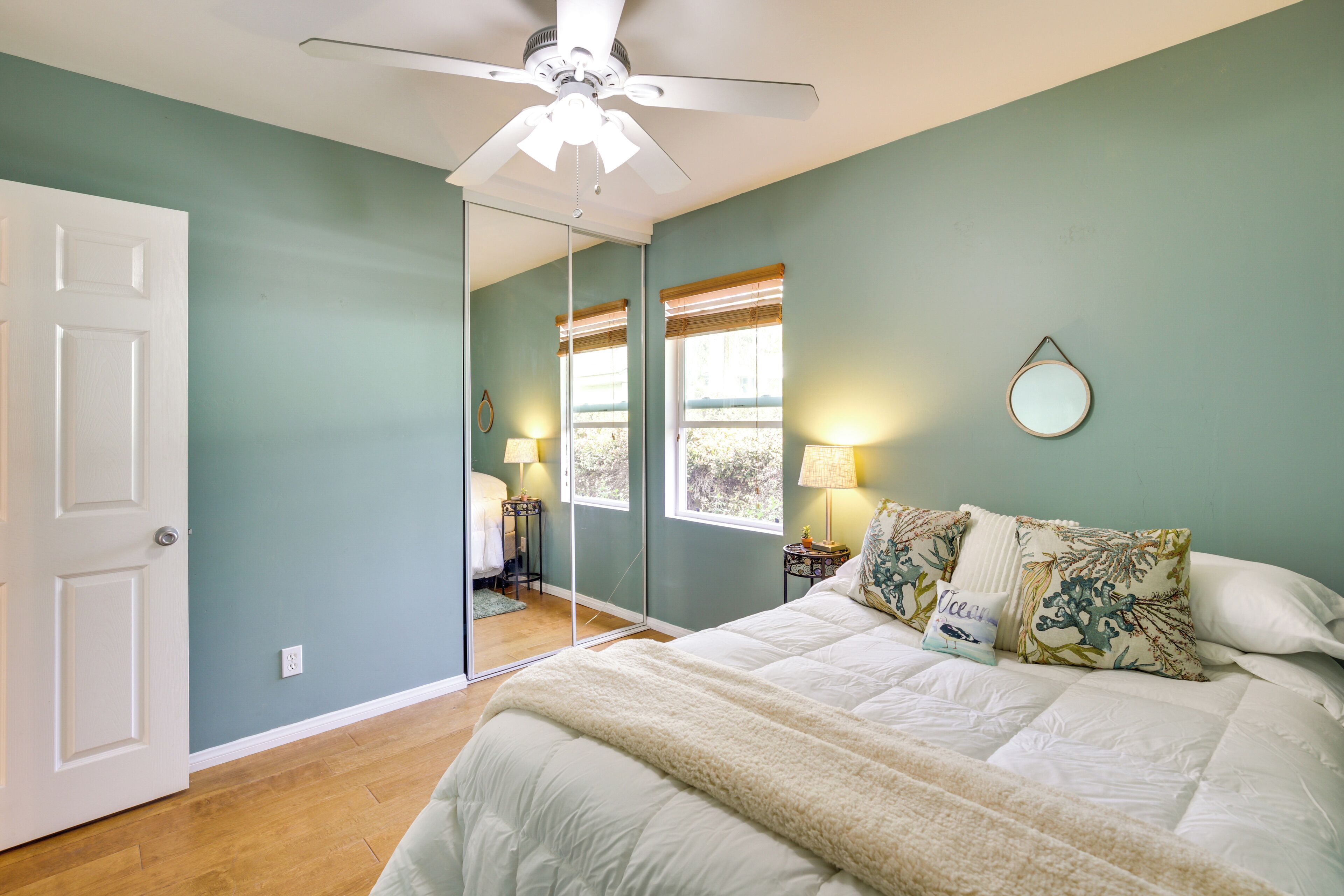 A bedroom with a bed, a ceiling fan, a mirror, and a window with blinds.