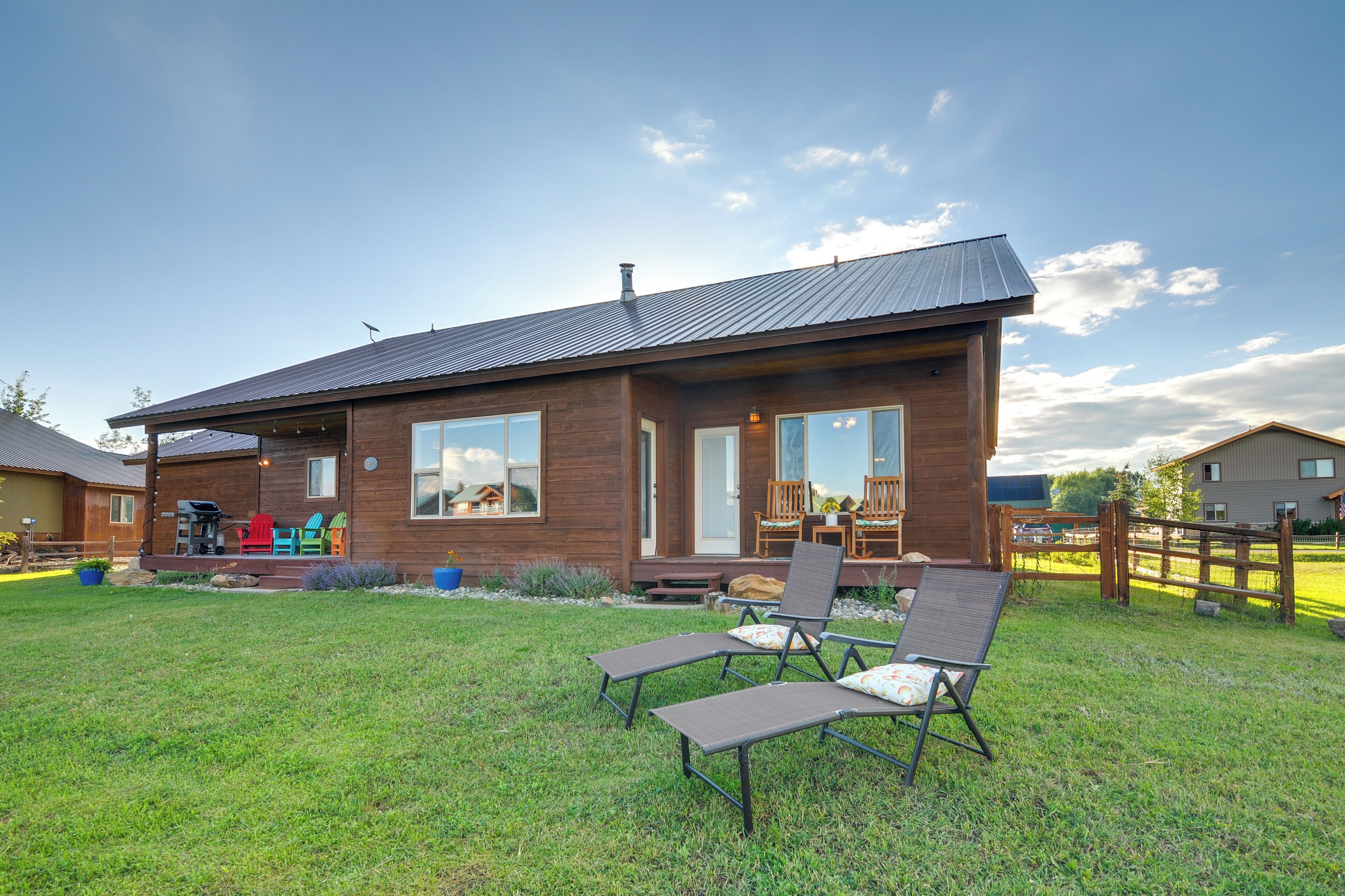 A modern house with a large deck, outdoor seating, and a well-maintained lawn.