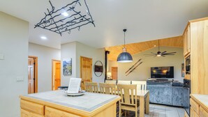 Eine moderne Küche mit Holdekor, einer zentralen Kochinsel, einem Essbereich mit Stühlen, einem Deckenventilator und einem Fernseher.