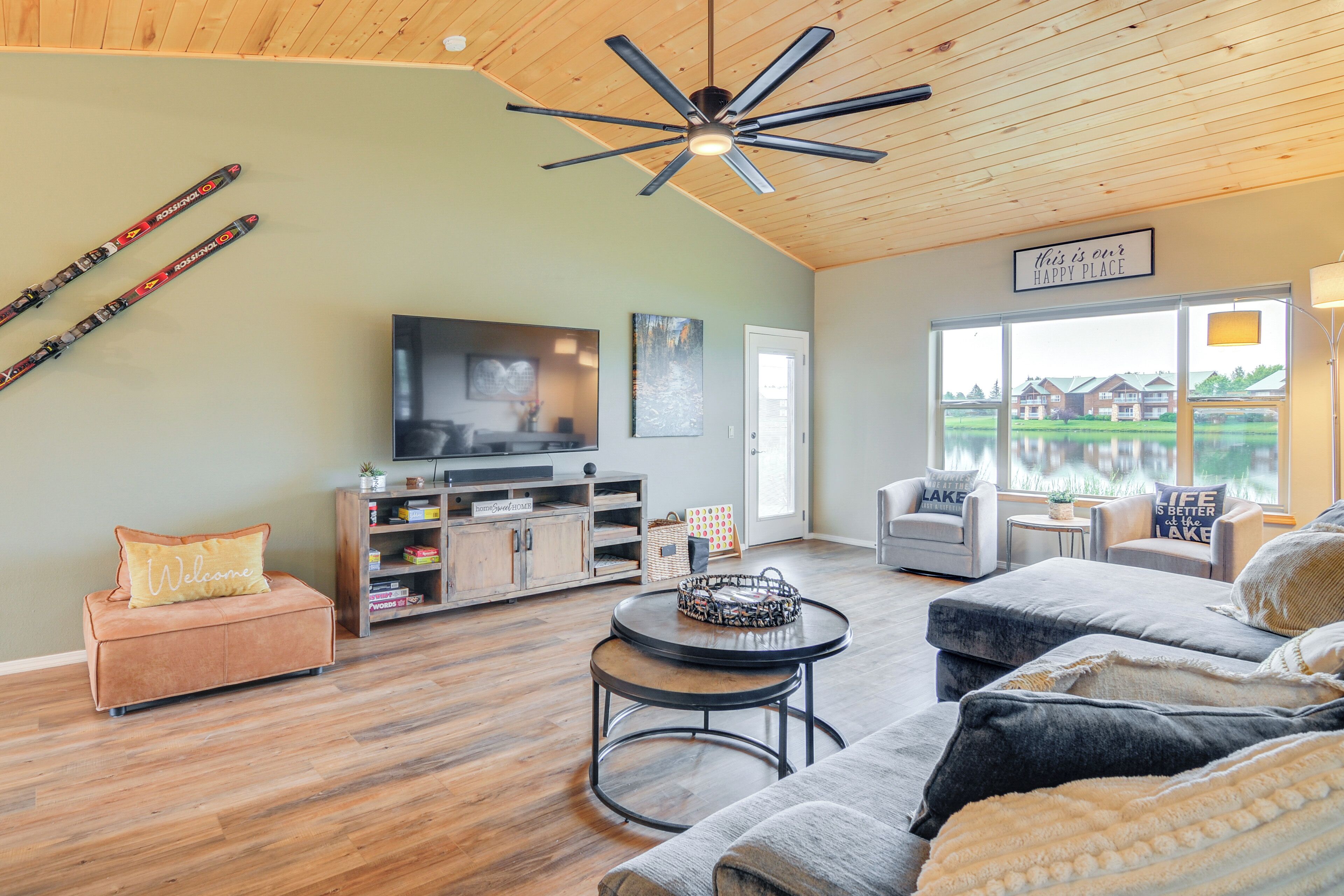 Amplia sala de estar con un televisor grande, techo de madera y vista a un lago.