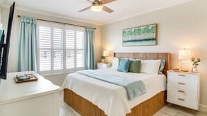 A bedroom with a bed, bedside tables, a ceiling fan, a window with curtains, and a painting on the wall. - Okaloosa Island Escape: Bayfront Condo Near Beach (Fort Walton Beach)