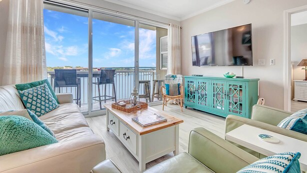 A living room with a sofa, coffee table, and a TV mounted on the wall. - Okaloosa Island Escape: Bayfront Condo Near Beach (Fort Walton Beach)