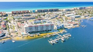 An aerial view of a coastal town with a marina, hotels, and a beach. - Okaloosa Island Escape: Bayfront Condo Near Beach (Fort Walton Beach)