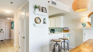 A kitchen with white cabinets, a wooden countertop, two stools, a hanging light fixture, and a mirror above the counter. - Okaloosa Island Escape: Bayfront Condo Near Beach (Fort Walton Beach)
